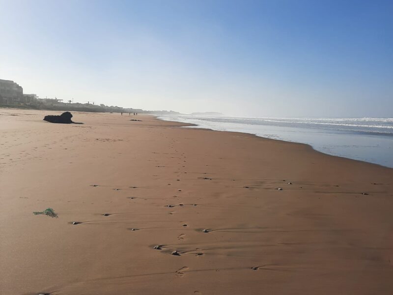 Weiter Sandstrand bei Tageslicht, auslaufende Wellen unter blauem Himmel